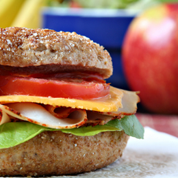 Healthy lunch, whole grain bagel with sliced turkey breast and fruit and vegetables.